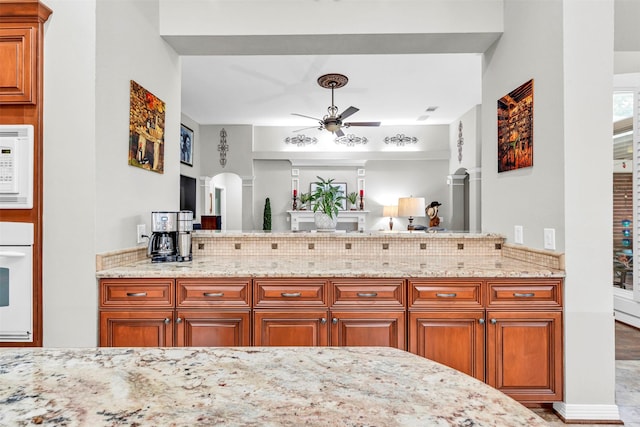 kitchen with light stone counters, white appliances, kitchen peninsula, and ceiling fan