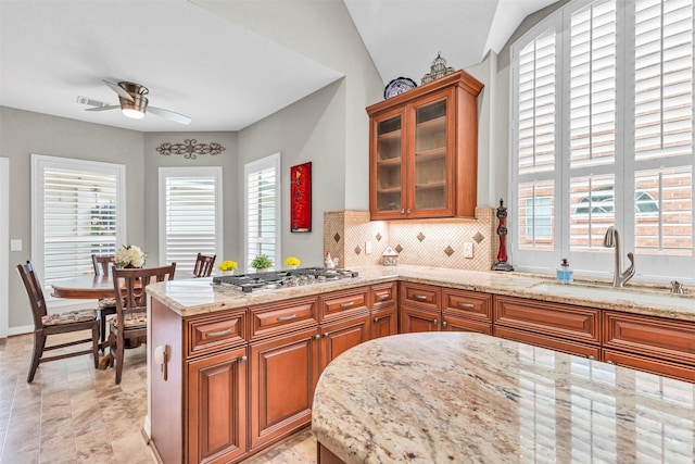 kitchen featuring sink, tasteful backsplash, ceiling fan, stainless steel gas stovetop, and light stone countertops