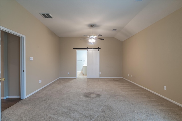 carpeted empty room featuring lofted ceiling, a barn door, and ceiling fan