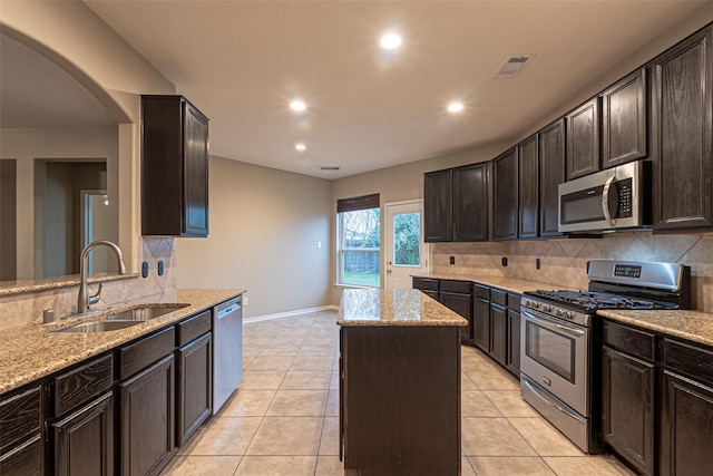 kitchen featuring appliances with stainless steel finishes, sink, light tile patterned flooring, light stone countertops, and a center island