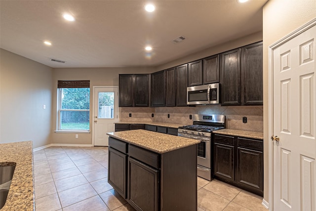 kitchen featuring light tile patterned floors, appliances with stainless steel finishes, dark brown cabinets, and a kitchen island