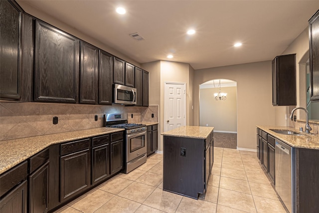 kitchen featuring a kitchen island, stainless steel appliances, sink, backsplash, and light stone counters