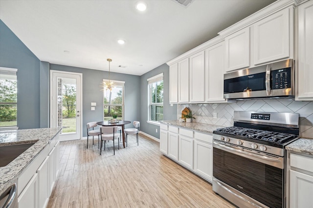 kitchen with light stone counters, white cabinets, backsplash, and appliances with stainless steel finishes