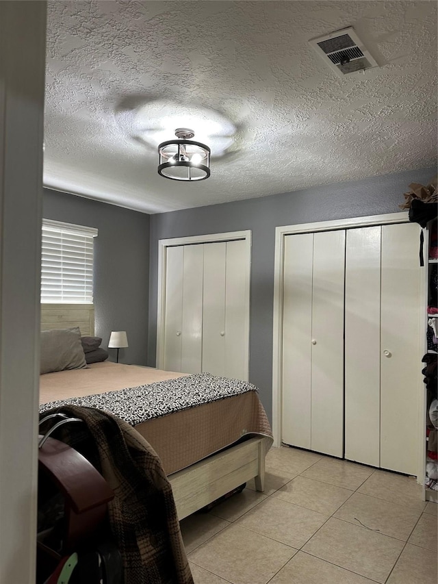 tiled bedroom with multiple closets and a textured ceiling