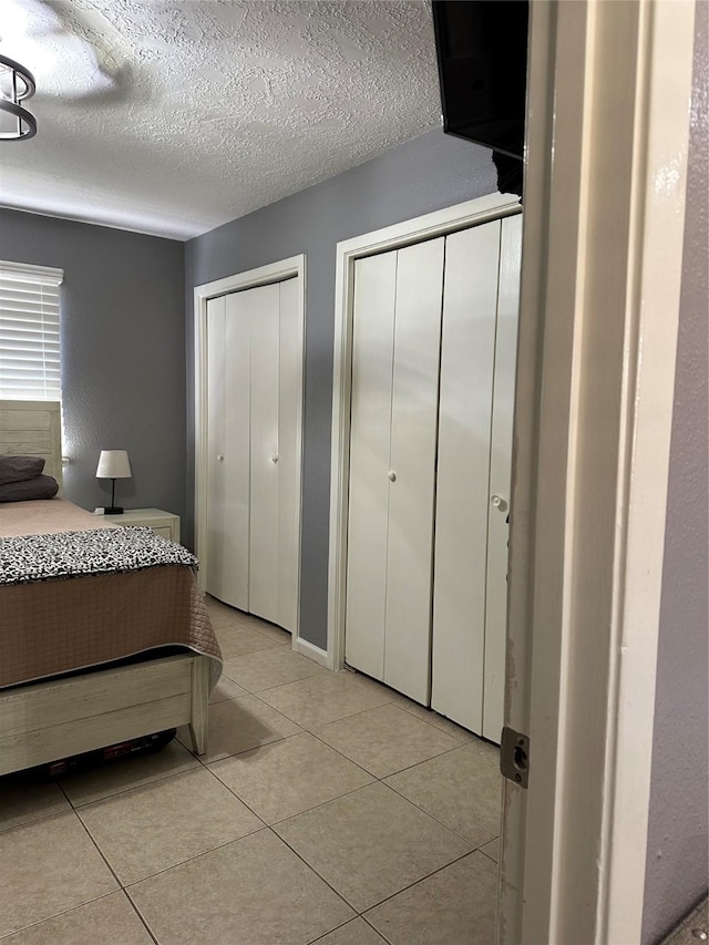 bedroom featuring light tile patterned flooring, a textured ceiling, and two closets