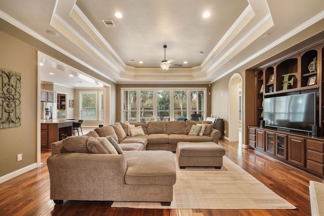 living room with ceiling fan, crown molding, a raised ceiling, and light wood-type flooring