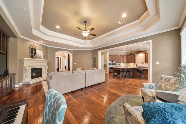 living room featuring crown molding, dark hardwood / wood-style floors, ceiling fan, and a raised ceiling