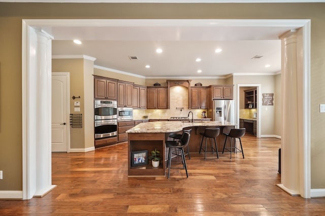 kitchen featuring tasteful backsplash, a spacious island, a breakfast bar, stainless steel appliances, and light stone counters