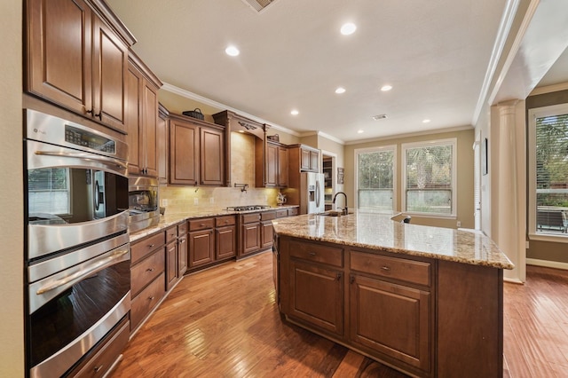 kitchen with light hardwood / wood-style flooring, sink, a kitchen island with sink, ornamental molding, and stainless steel appliances