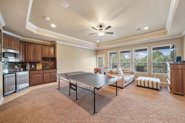 playroom with ceiling fan, a raised ceiling, ornamental molding, and light carpet