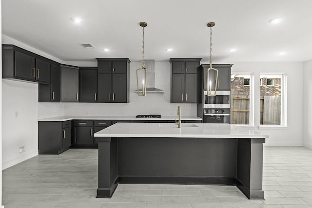 kitchen featuring wall chimney exhaust hood, light stone countertops, sink, and a center island with sink