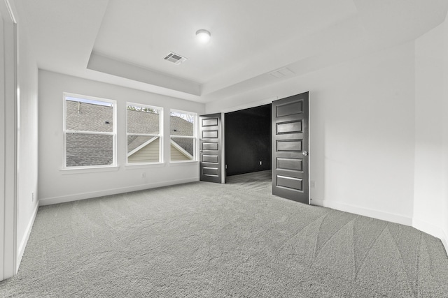 unfurnished bedroom with a tray ceiling and carpet