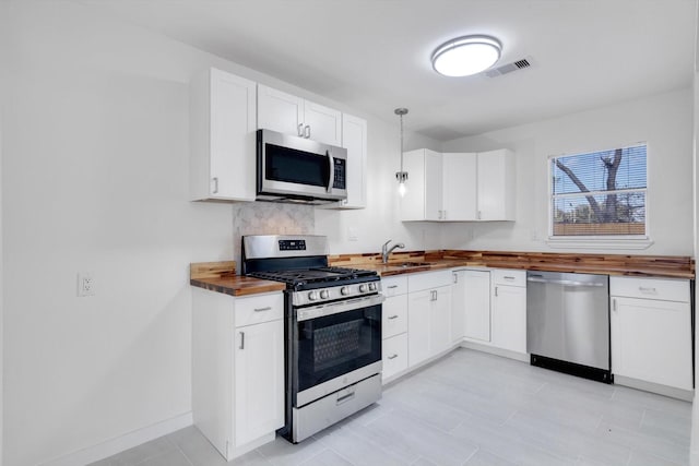 kitchen with white cabinets, wooden counters, decorative light fixtures, stainless steel appliances, and backsplash