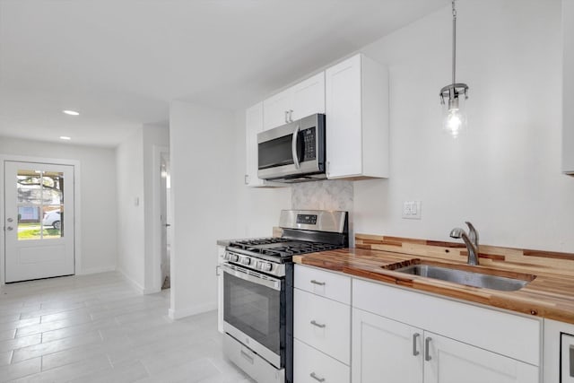 kitchen with decorative light fixtures, butcher block countertops, sink, white cabinetry, and stainless steel appliances