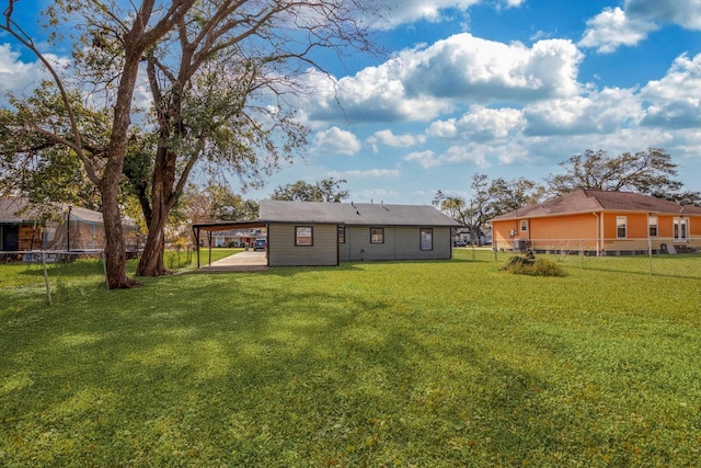 rear view of property featuring a yard, a carport, and a trampoline