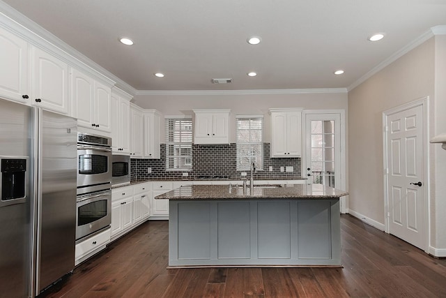 kitchen featuring white cabinetry, stainless steel appliances, dark stone countertops, and a center island with sink