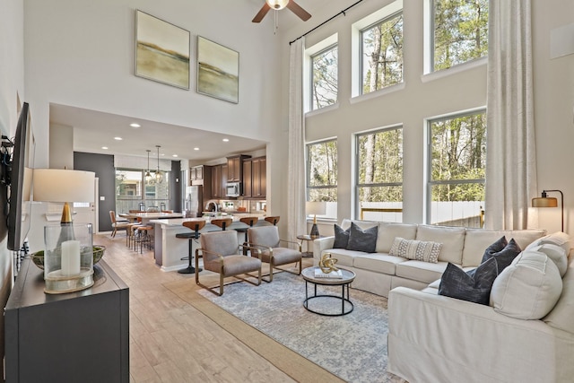 living room featuring ceiling fan, light hardwood / wood-style flooring, and a towering ceiling