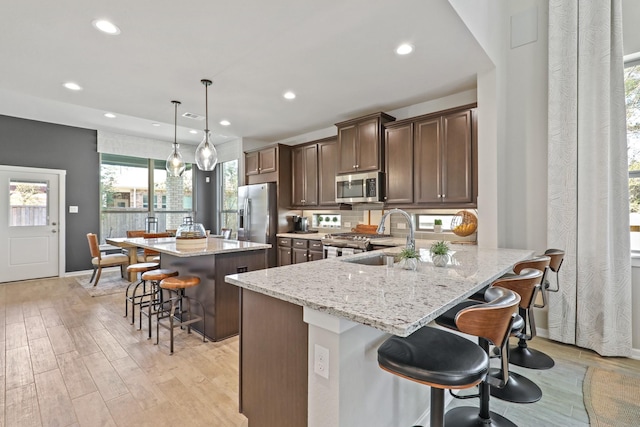 kitchen with a kitchen bar, a center island with sink, stainless steel appliances, light stone countertops, and sink