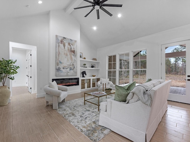 living area featuring baseboards, a glass covered fireplace, beamed ceiling, light wood-type flooring, and high vaulted ceiling