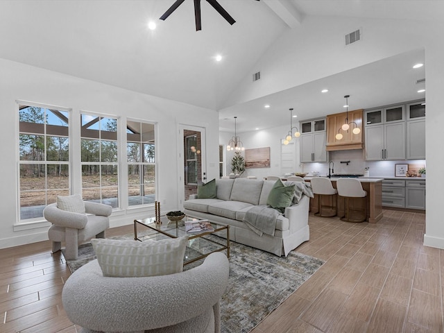 living room with sink, ceiling fan with notable chandelier, high vaulted ceiling, and beamed ceiling