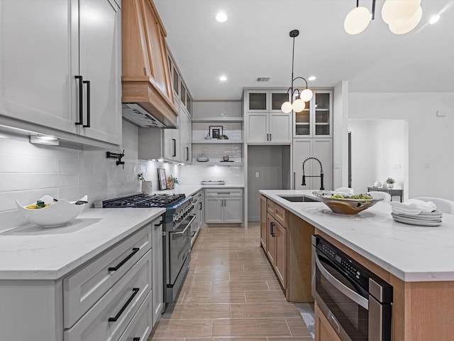 kitchen featuring pendant lighting, light stone counters, stainless steel stove, and an island with sink