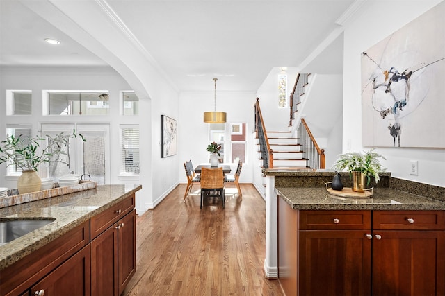 kitchen with pendant lighting, sink, dark stone countertops, ornamental molding, and light wood-type flooring