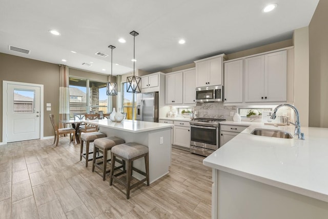 kitchen with appliances with stainless steel finishes, decorative light fixtures, a kitchen island, white cabinets, and sink