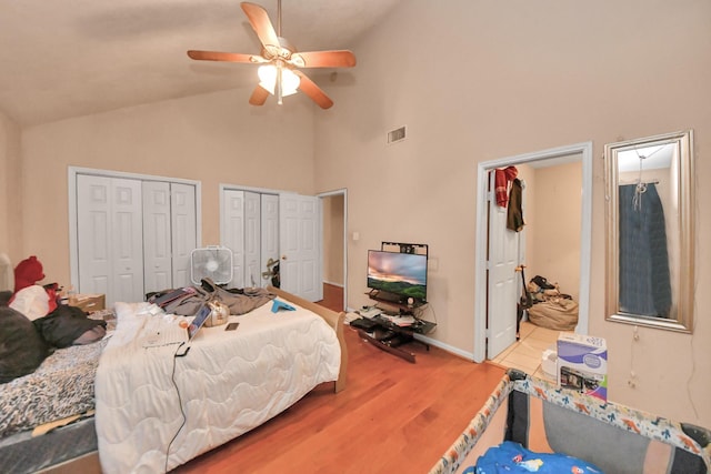 bedroom featuring ceiling fan, hardwood / wood-style flooring, multiple closets, and high vaulted ceiling