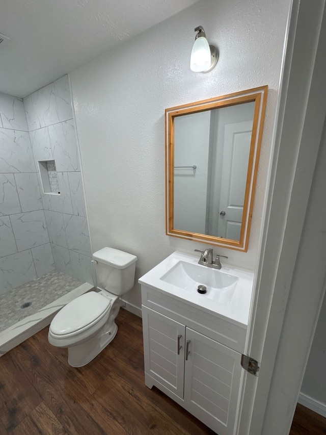 bathroom featuring wood-type flooring, toilet, vanity, and tiled shower