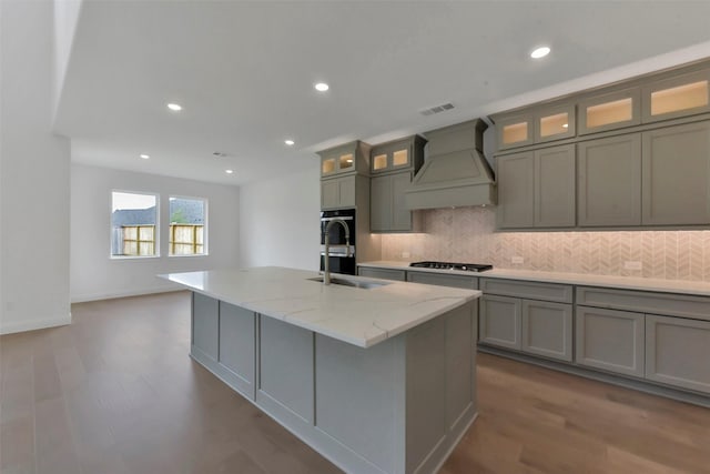13115 Brookwood Bend Ln, Conroe, TX 77302 - kitchen with custom exhaust hood, a sink, a kitchen island with sink, backsplash, and dark wood-style flooring