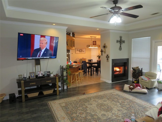 living room with ceiling fan, dark wood-type flooring, a tray ceiling, and ornamental molding