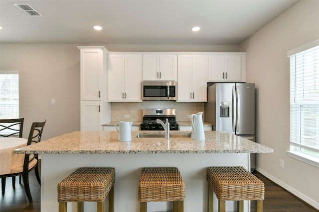 kitchen featuring a center island with sink, appliances with stainless steel finishes, backsplash, and white cabinetry