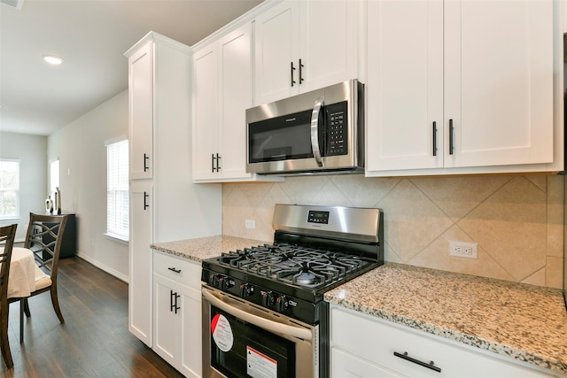 kitchen featuring light stone countertops, white cabinets, appliances with stainless steel finishes, dark wood-type flooring, and backsplash