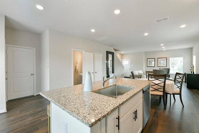 kitchen featuring sink, white cabinetry, dark wood-type flooring, an island with sink, and light stone counters