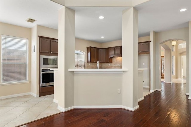 kitchen featuring appliances with stainless steel finishes, tasteful backsplash, dark brown cabinetry, kitchen peninsula, and light hardwood / wood-style floors