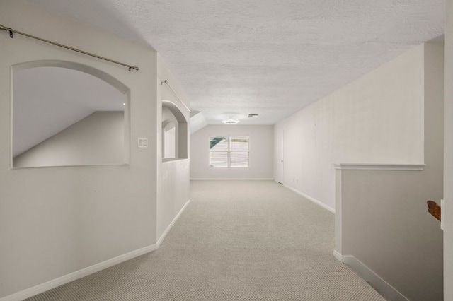 corridor with lofted ceiling, light colored carpet, and a textured ceiling