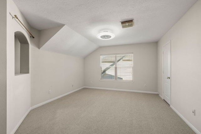 additional living space with light colored carpet, vaulted ceiling, and a textured ceiling