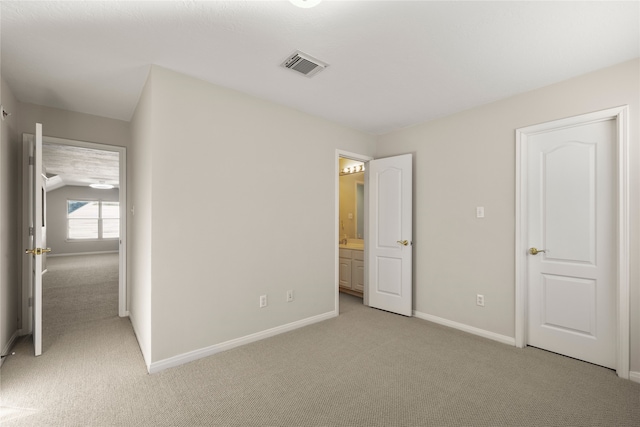 unfurnished bedroom featuring vaulted ceiling, connected bathroom, and light colored carpet