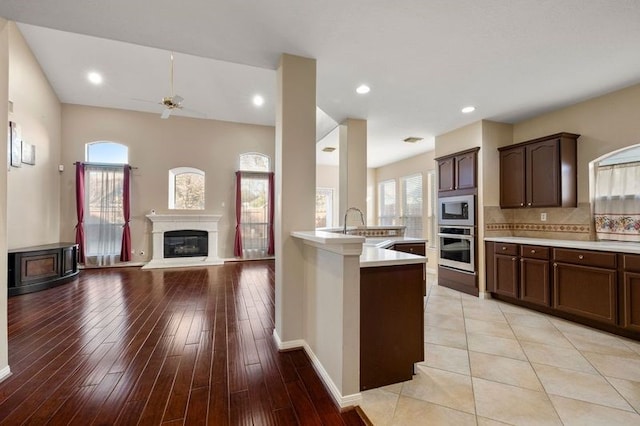 kitchen featuring built in microwave, dark brown cabinetry, sink, stainless steel oven, and decorative backsplash