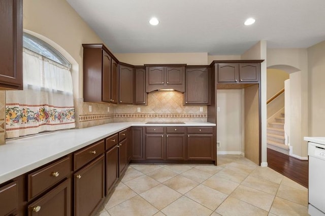 kitchen featuring light tile patterned flooring, tasteful backsplash, dark brown cabinetry, white dishwasher, and black electric cooktop