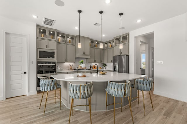 kitchen featuring appliances with stainless steel finishes, a kitchen island with sink, light wood-type flooring, a kitchen breakfast bar, and pendant lighting