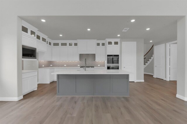 16163 Sheridan River Trl, Conroe, TX 77302 - kitchen featuring decorative backsplash, light wood-style flooring, a spacious island, white cabinets, and appliances with stainless steel finishes