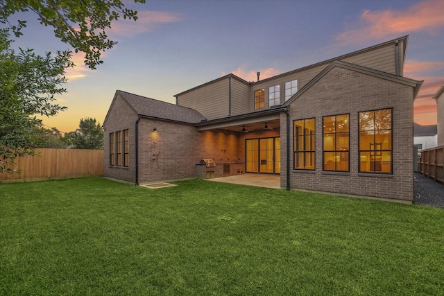 back house at dusk featuring ceiling fan, a yard, and a patio