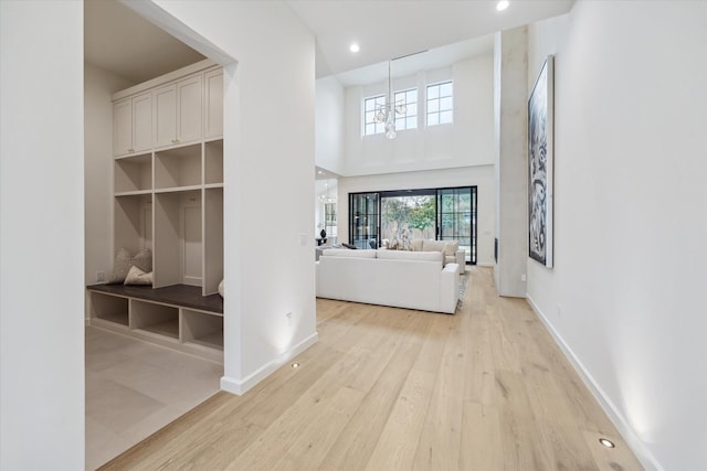 corridor featuring a towering ceiling, light hardwood / wood-style flooring, and a chandelier