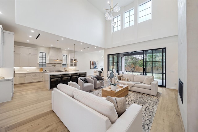 living room with light hardwood / wood-style floors, a towering ceiling, and a notable chandelier