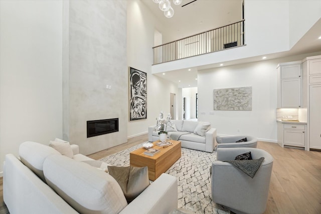 living room with a large fireplace, light hardwood / wood-style flooring, and a towering ceiling