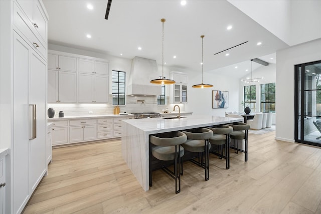 kitchen featuring custom range hood, pendant lighting, a large island with sink, white cabinets, and a breakfast bar