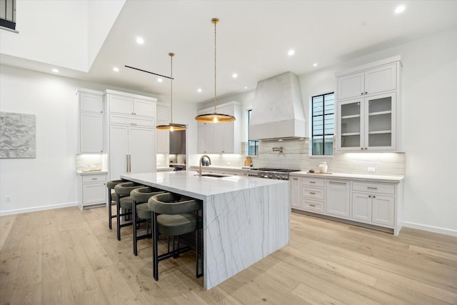 kitchen featuring a spacious island, decorative light fixtures, white cabinetry, sink, and custom range hood