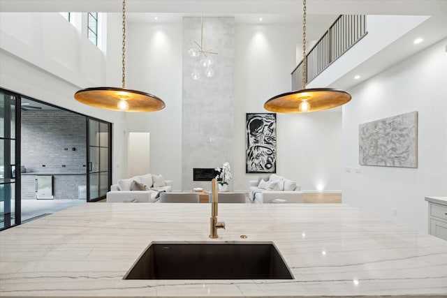 kitchen with a high ceiling, light stone countertops, decorative light fixtures, sink, and a large fireplace