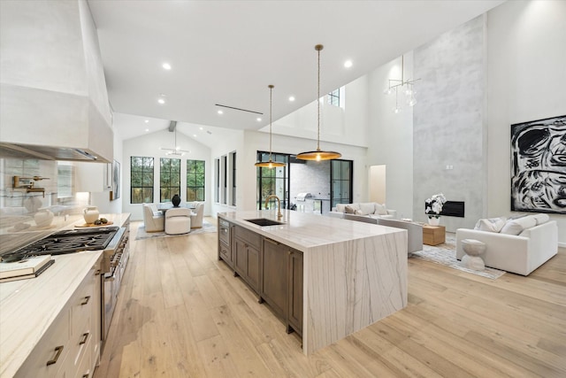 kitchen with hanging light fixtures, sink, high vaulted ceiling, an island with sink, and double oven range